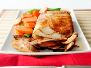 A serving of crispy baked fish with sautéed carrots and snap peas, accompanied by homemade potato chips on a white plate.