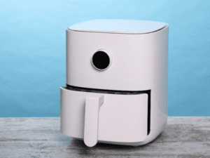 A sleek, white air fryer with an open basket, placed on a wooden surface against a blue background.