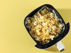 Freshly popped popcorn inside an air fryer basket on a yellow background.
