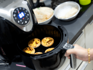 A black air fryer cooking four golden tarts on a kitchen counter.
