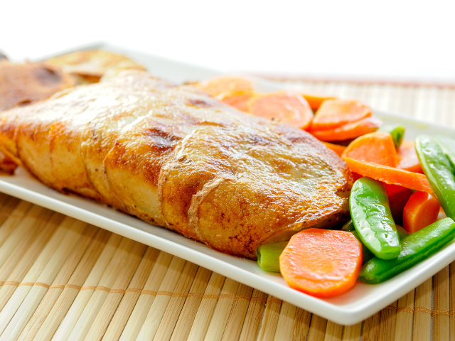 Close-up of a crispy baked fish fillet served with carrots and snap peas on a white rectangular plate.