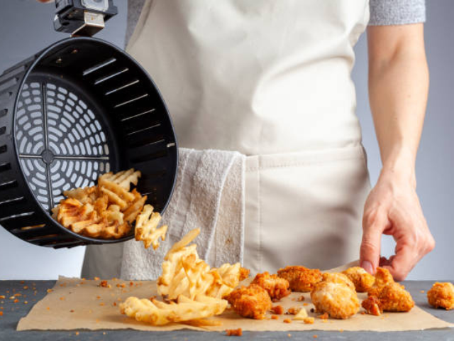 Close-up view of a person pouring fries and chicken nuggets from an air fryer basket onto a tray.
