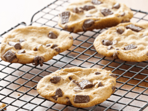 Four freshly baked chocolate chip cookies resting on a cooling rack, ready to enjoy.