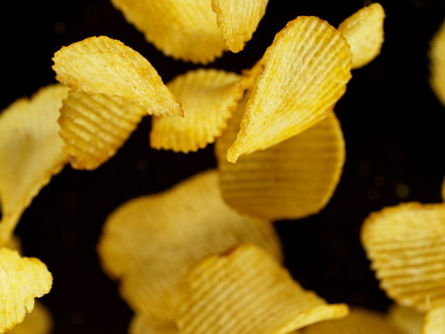Crinkled potato chips falling in midair against a dark background.