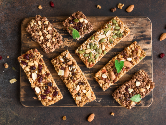 A variety of granola bars topped with seeds, nuts, and dried fruits displayed on a rustic wooden board.