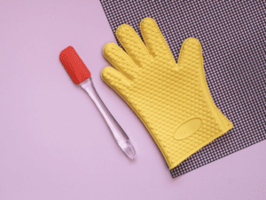 A yellow oven mitt and a red spatula placed on a purple background, essential baking tools.