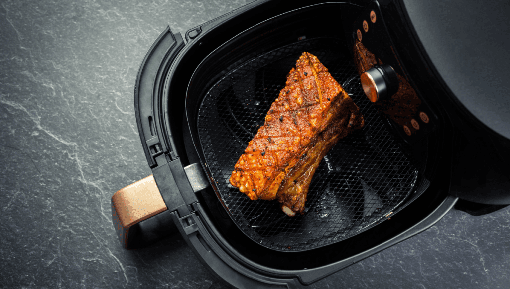 A perfectly grilled piece of seasoned pork belly with crispy skin sitting inside an air fryer basket.
