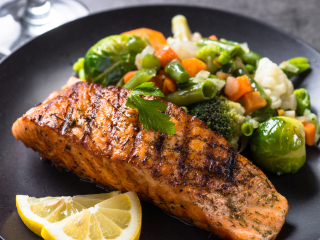 Grilled salmon fillet served with a side of mixed vegetables and a lemon wedge.