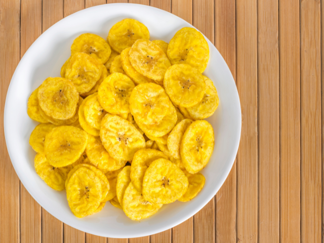 A plate of crispy golden plantain chips on a bamboo-textured surface.