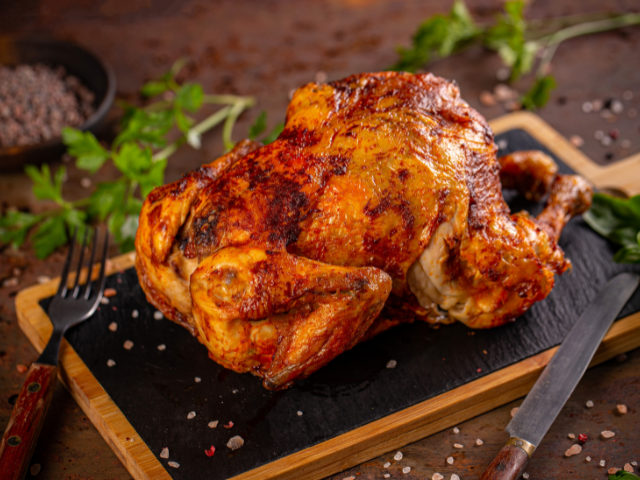 Whole roasted chicken with crispy skin served on a cutting board with herbs.