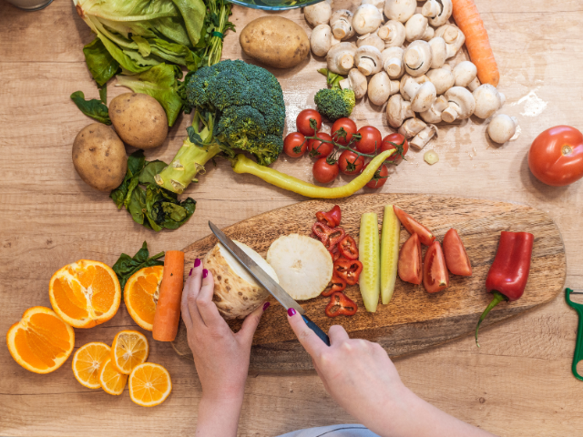 A person preparing a vibrant assortment of fresh vegetables, including tomatoes, broccoli, carrots, and mushrooms, on a wooden cutting board.