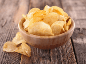 A wooden bowl filled with golden potato chips on a rustic wooden surface.