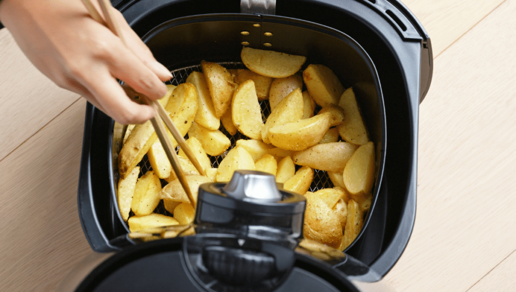 A person using chopsticks to stir potato wedges cooking in an air fryer.