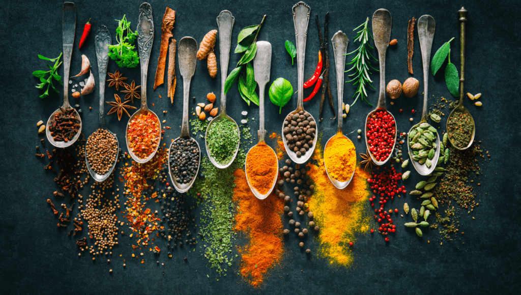 A vibrant display of various spices arranged in wooden spoons on a dark background, showing a variety of colorful spices like black pepper, red chili flakes, and turmeric.