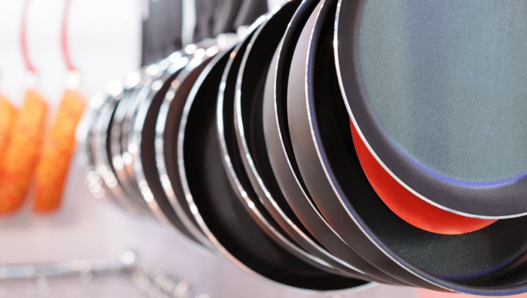 A row of nonstick pans hanging on display, showcasing their sleek surfaces and variety in size. These pans are arranged in a visually appealing way, emphasizing their practical use in cooking.