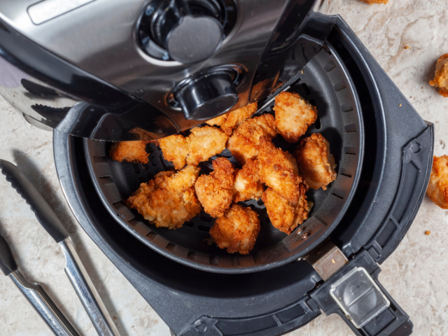 Chicken nuggets inside an air fryer basket with tongs beside it.