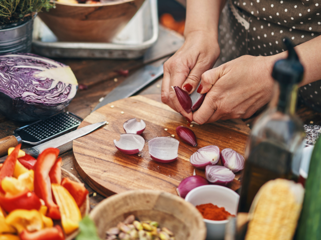 Hands preparing fresh vegetables, including onions and bell peppers, on a wooden cutting board for a meal.