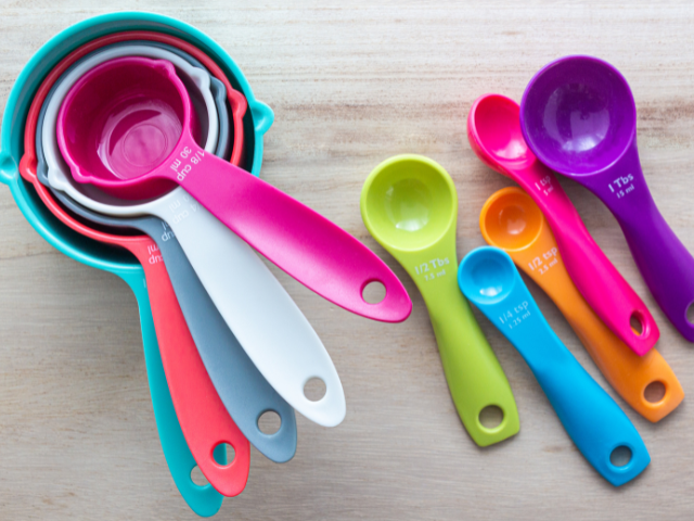 olorful plastic measuring spoons and cups arranged on a wooden surface.