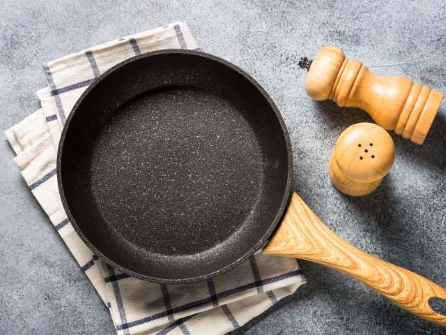 A black nonstick frying pan resting on a rustic surface with a checkered cloth beneath.