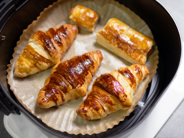 Flaky golden croissants and pastries inside an air fryer.