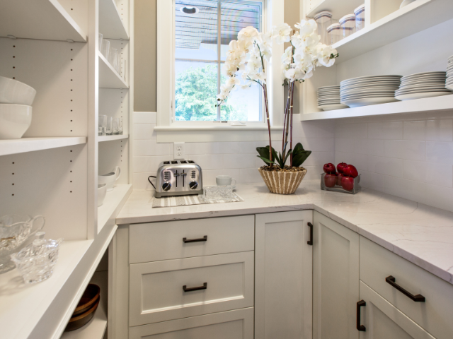 A bright pantry with white shelves, neatly arranged dishes, and appliances.