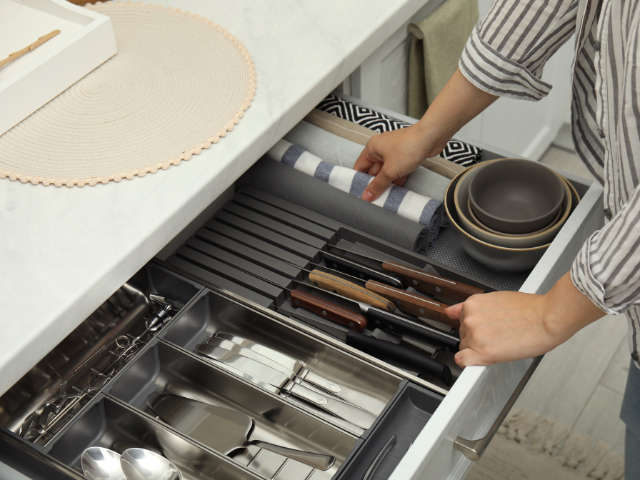 Person organizing knives and utensils in a kitchen drawer.