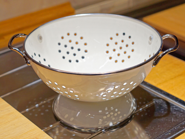 White metal colander with handles placed in a kitchen sink.