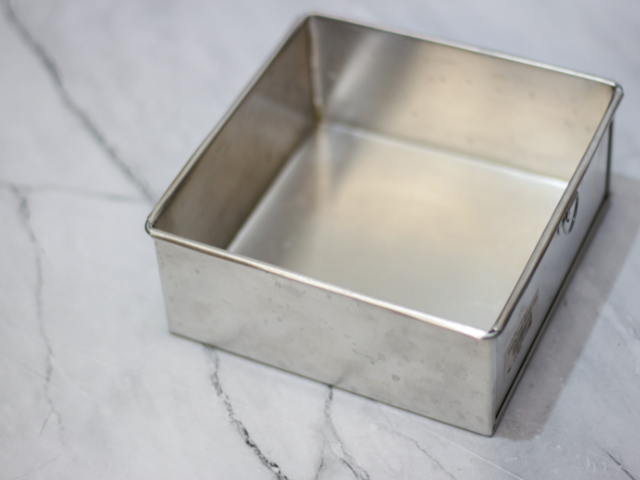 A square metal baking pan placed on a marble countertop, ready for baking.
