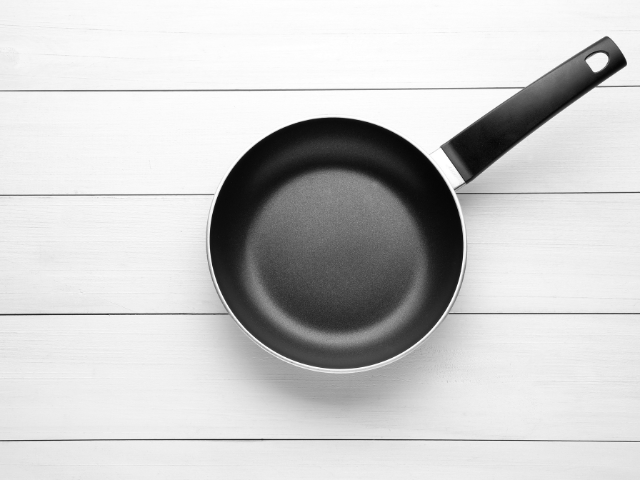 A simple, sleek black frying pan on a white wooden background, highlighting the modern and minimalist design.