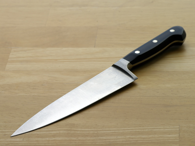 A sharp kitchen knife on a wooden countertop.