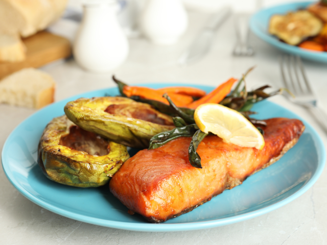 Grilled salmon served with roasted vegetables on a blue plate.