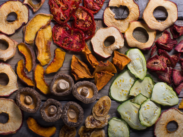 A variety of dried vegetables and fruits, including tomatoes, mushrooms, apples, and zucchinis, arranged on a wooden surface.