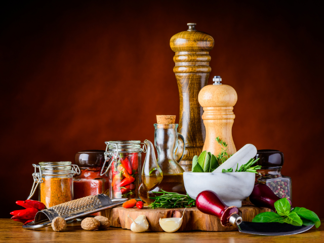 A rustic kitchen setup with jars of spices, herbs, and classic wooden pepper mills.